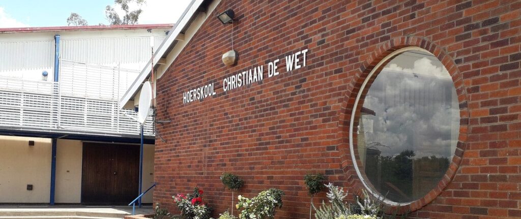 High school building with brick walls and large round window, Christian De Wet High School, South African educational institution, school exterior, educational campus, school facilities.