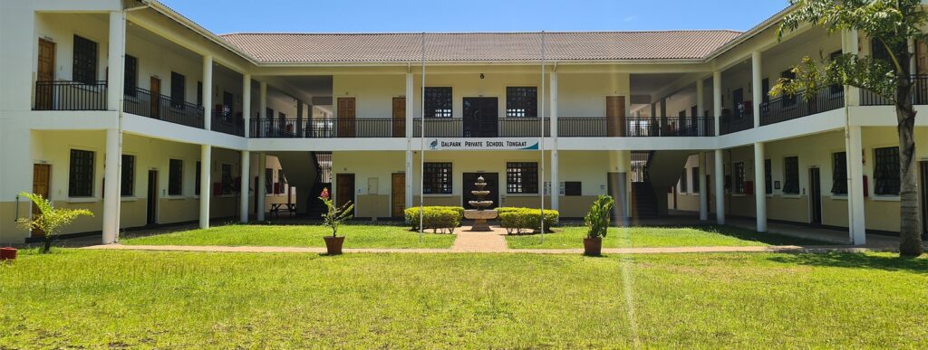 Modern private school building with lush green lawn, sign indicating Dalpark Private School Tongaat in South Africa, featuring two floors, student facilities, and well-maintained surroundings.